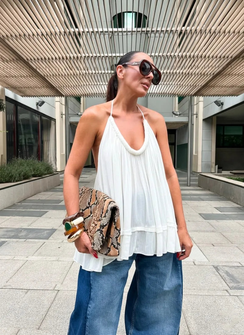 Woman in a white top and blue jeans holding a patterned clutch outdoors.