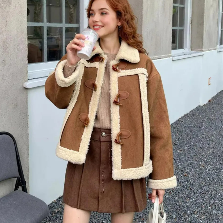 Woman wearing a brown coat with white fur trim, holding a cup outdoors.
