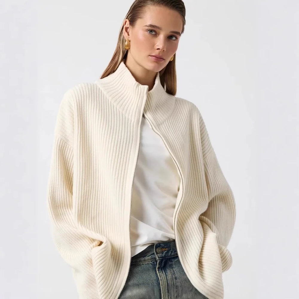 Woman wearing a cream-colored sweater over a white shirt with a plain background