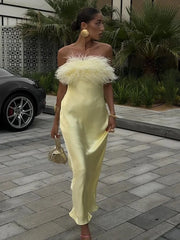 Woman in a yellow dress with feathered top standing on a paved area with plants in the background