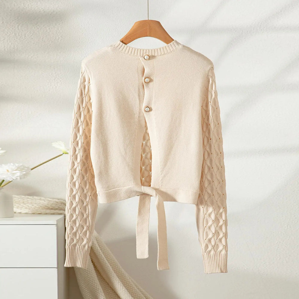 Beige cardigan with cable knit sleeves on a wooden hanger against a white background