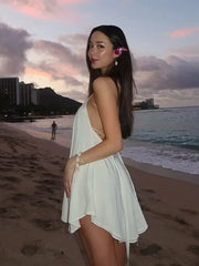 Woman in a white dress standing on a beach with a cityscape in the background