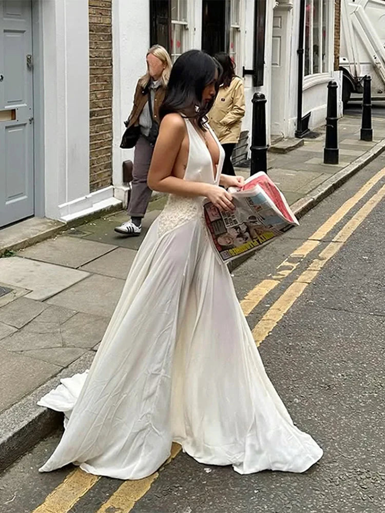 Woman in a white dress reading a newspaper on a street.