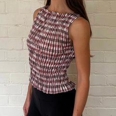 Person wearing a plaid sleeveless top against a white brick wall