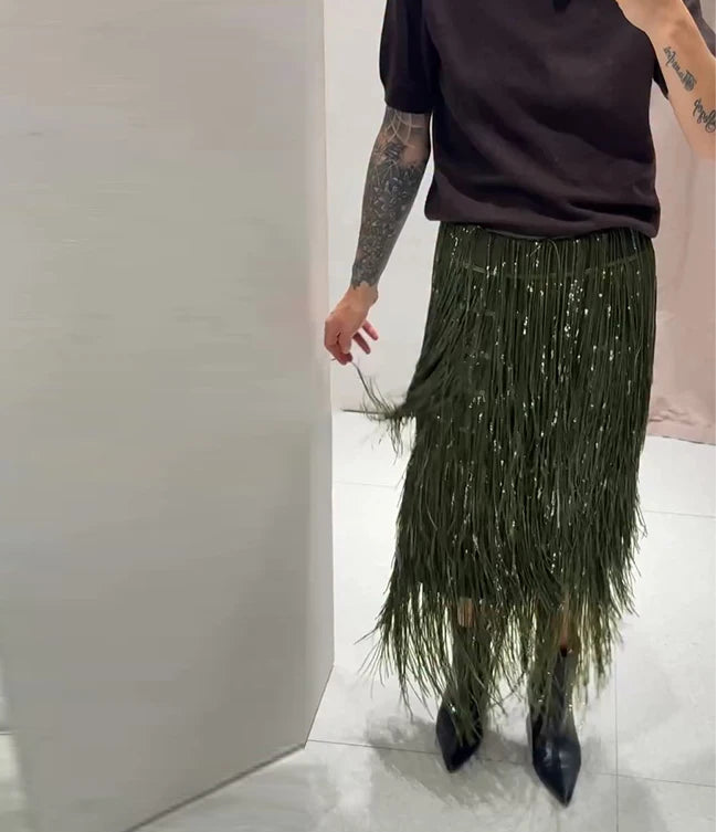 Person wearing a dark top and green fringe skirt in an indoor setting