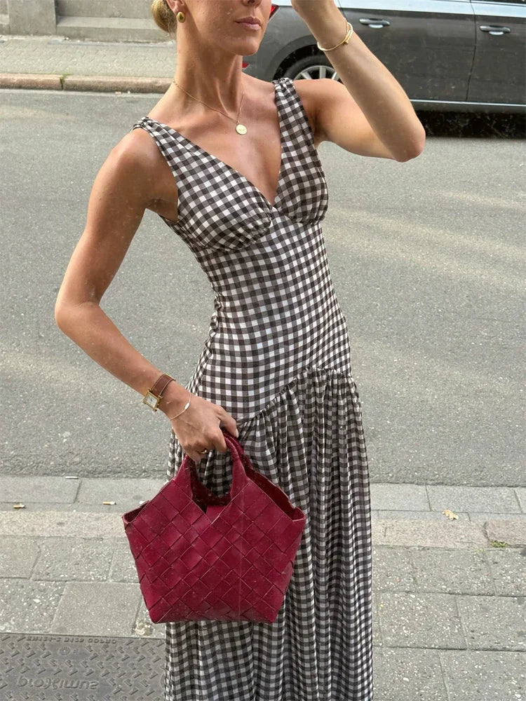 Woman in a checkered dress holding a red bag on a street.