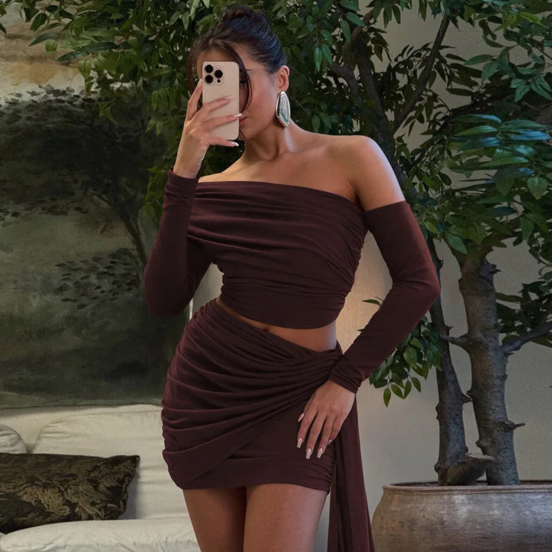 Woman taking a mirror selfie wearing a brown off-shoulder dress in a room with plants.