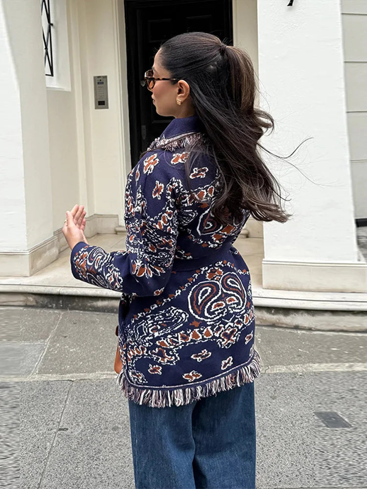 Woman wearing a patterned jacket and jeans walking outdoors.