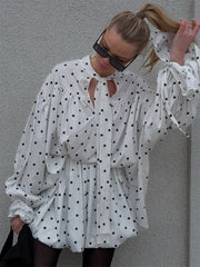 Woman wearing a white polka dot dress against a gray wall