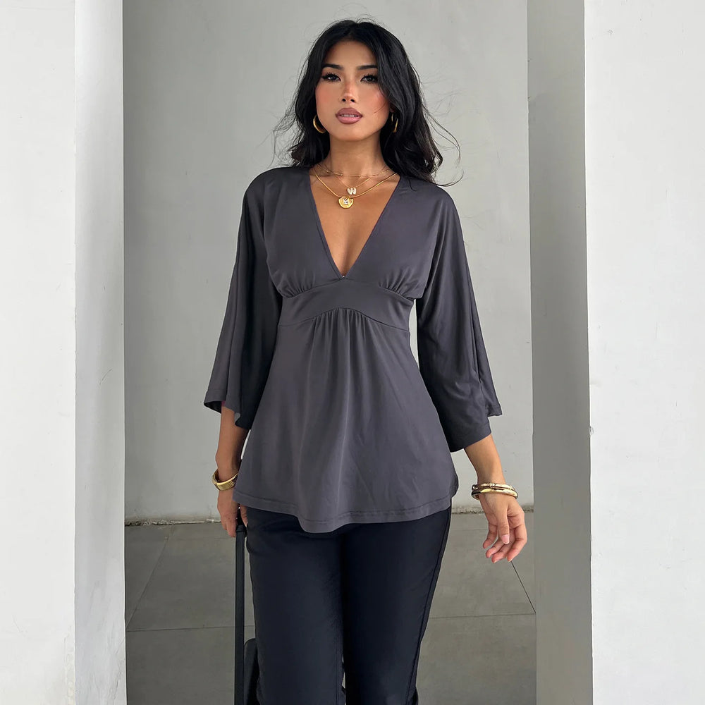 Woman wearing a gray blouse and black pants against a plain background