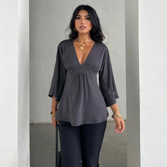 Woman wearing a gray blouse and black pants against a plain background