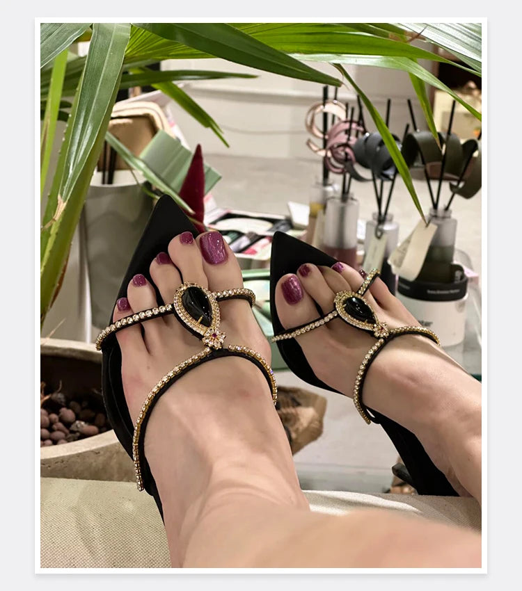 Black high-heeled sandals with gold detailing worn indoors.