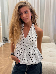 Woman wearing a white top with black polka dots in a room with light-colored curtains.