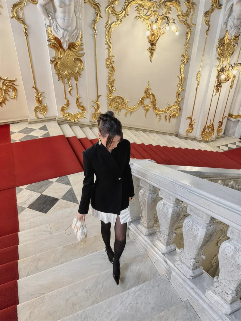 Woman in a black coat walking down a grand staircase with ornate gold decorations.