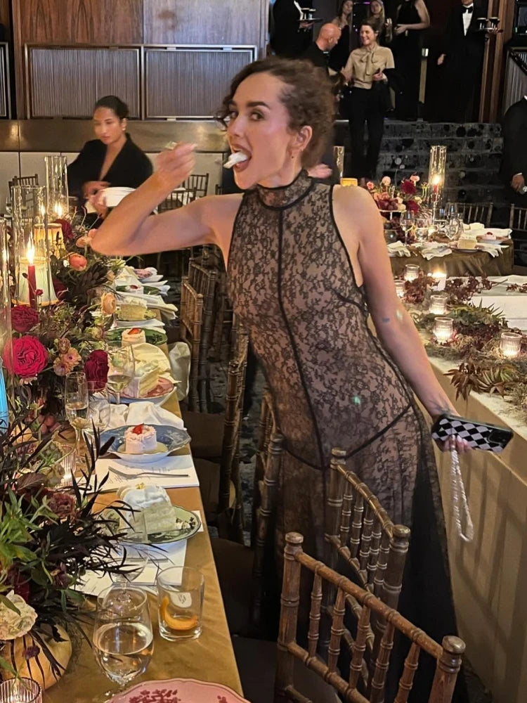 Woman in a lace dress standing at a formal event with tables and guests in the background.