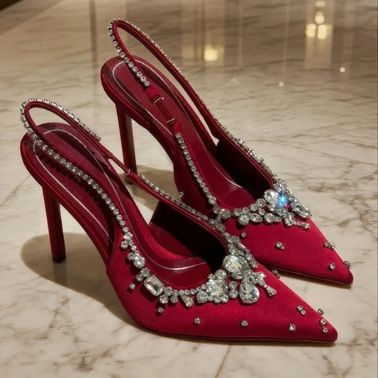 Red pointed toe slingback pumps with crystal embellishments on a marble floor