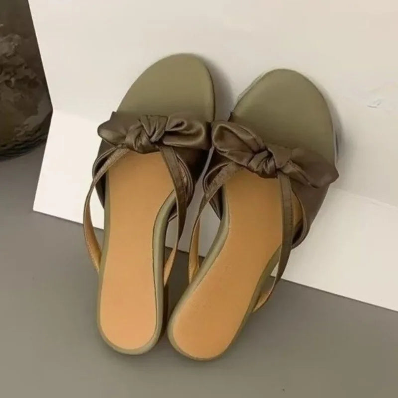 Pair of green sandals with brown ribbons on a white and gray background