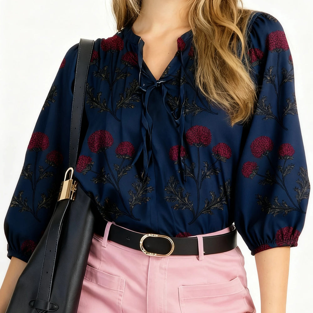 Woman wearing a navy blouse with red floral patterns and pink pants, holding a black bag.