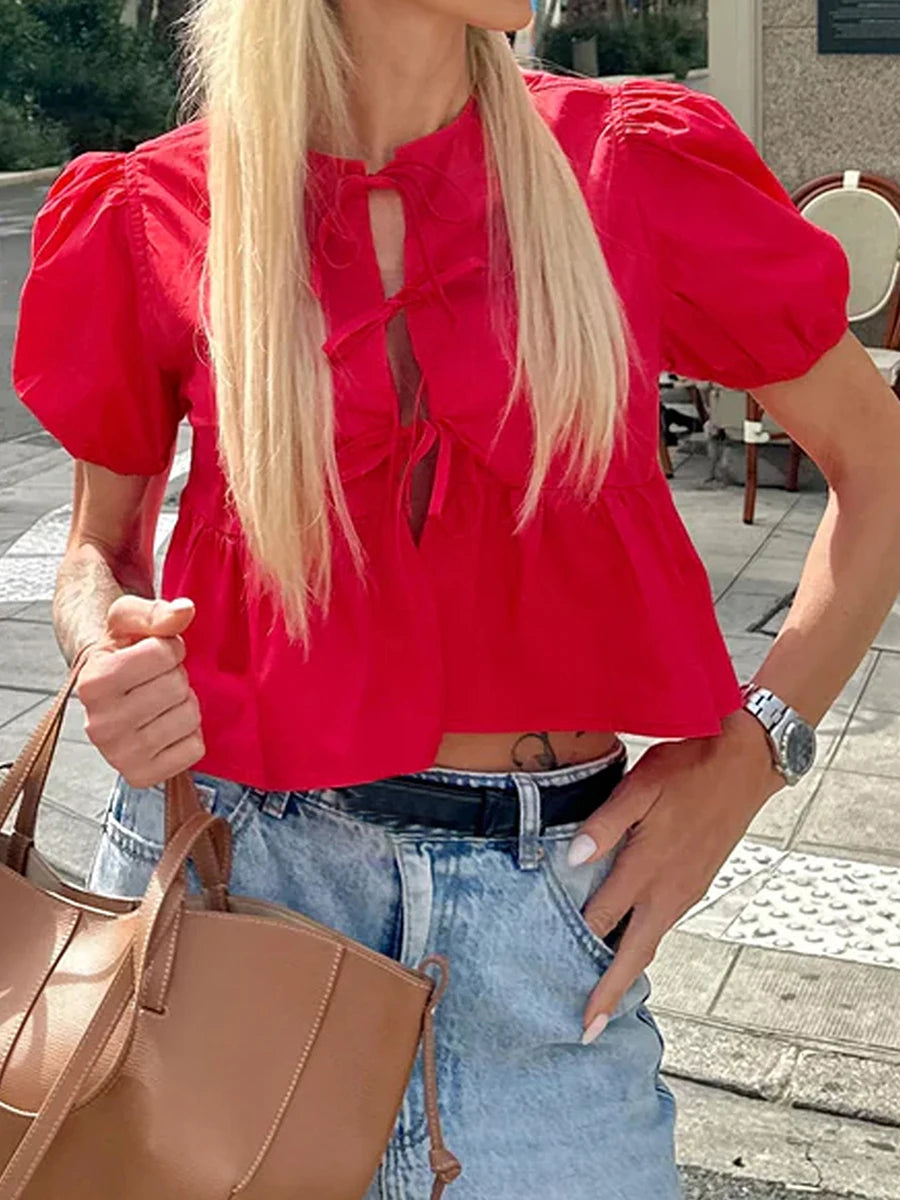 Person wearing a bright red blouse with puff sleeves and blue jeans, holding a brown bag.