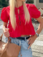 Person wearing a bright red blouse with puff sleeves and blue jeans, holding a brown bag.