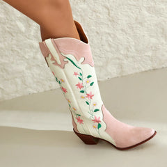 Pink cowboy boots with floral embroidery on a textured surface