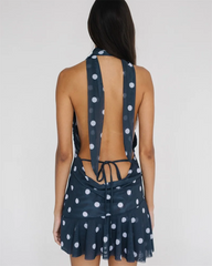 Navy blue dress with white polka dots featuring a halter neck and tied back design on a plain background.