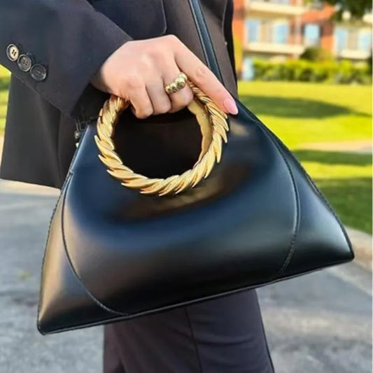 Black triangular top handle bag with a gold sculptural ring handle
