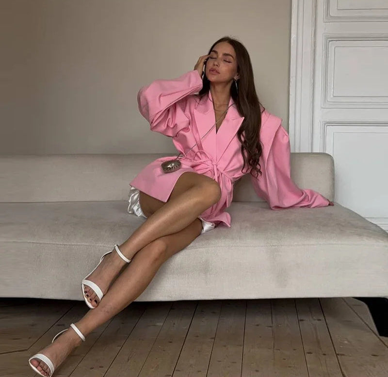 Woman in a pink robe sitting on a couch in a room with wooden flooring.