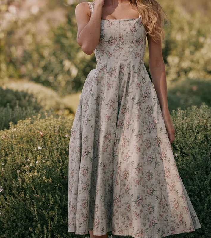 Woman wearing a vintage floral prairie dress with square neckline and mid-calf length in a countryside garden.

