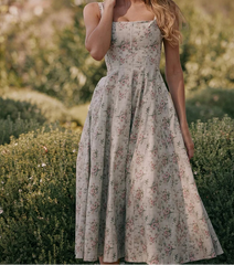 Woman wearing a vintage floral prairie dress with square neckline and mid-calf length in a countryside garden.
