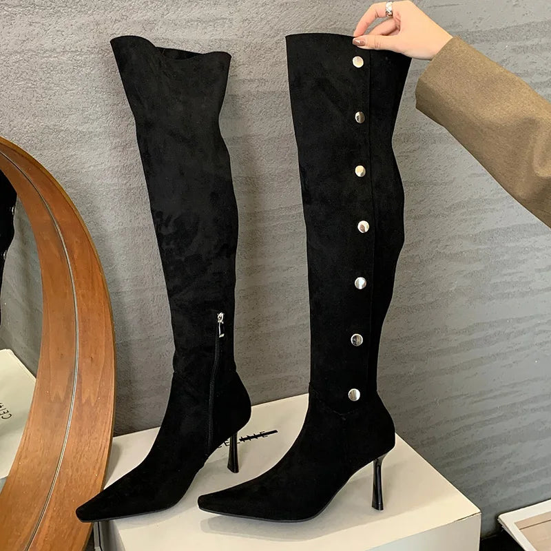 Black knee-high boots with silver buttons on a gray surface
