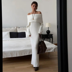 Woman in a white off-shoulder top and pants standing in a bedroom.