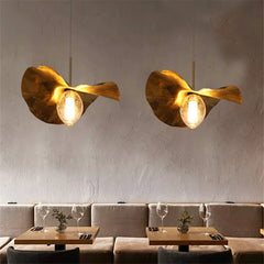 A minimalist brass lotus leaf pendant light casting a warm glow over a modern dining table. A