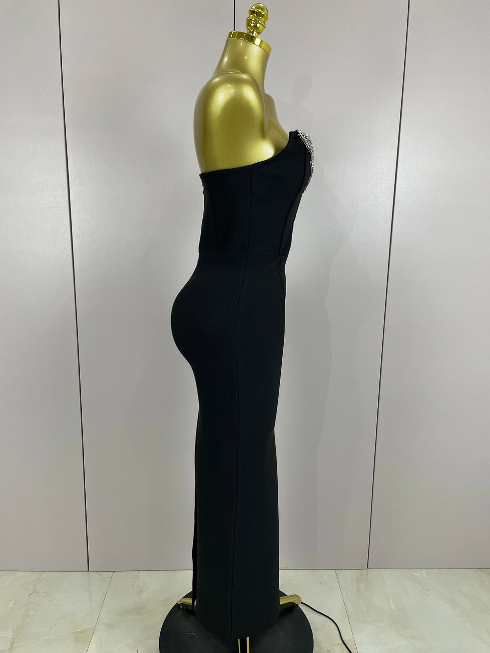 Black one-shoulder dress on a gold mannequin against a plain background