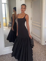 Woman in a black evening gown standing in a room with a mirror reflection.