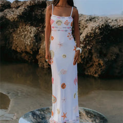 Woman in a floral dress standing on a beach with large rocks in the background
