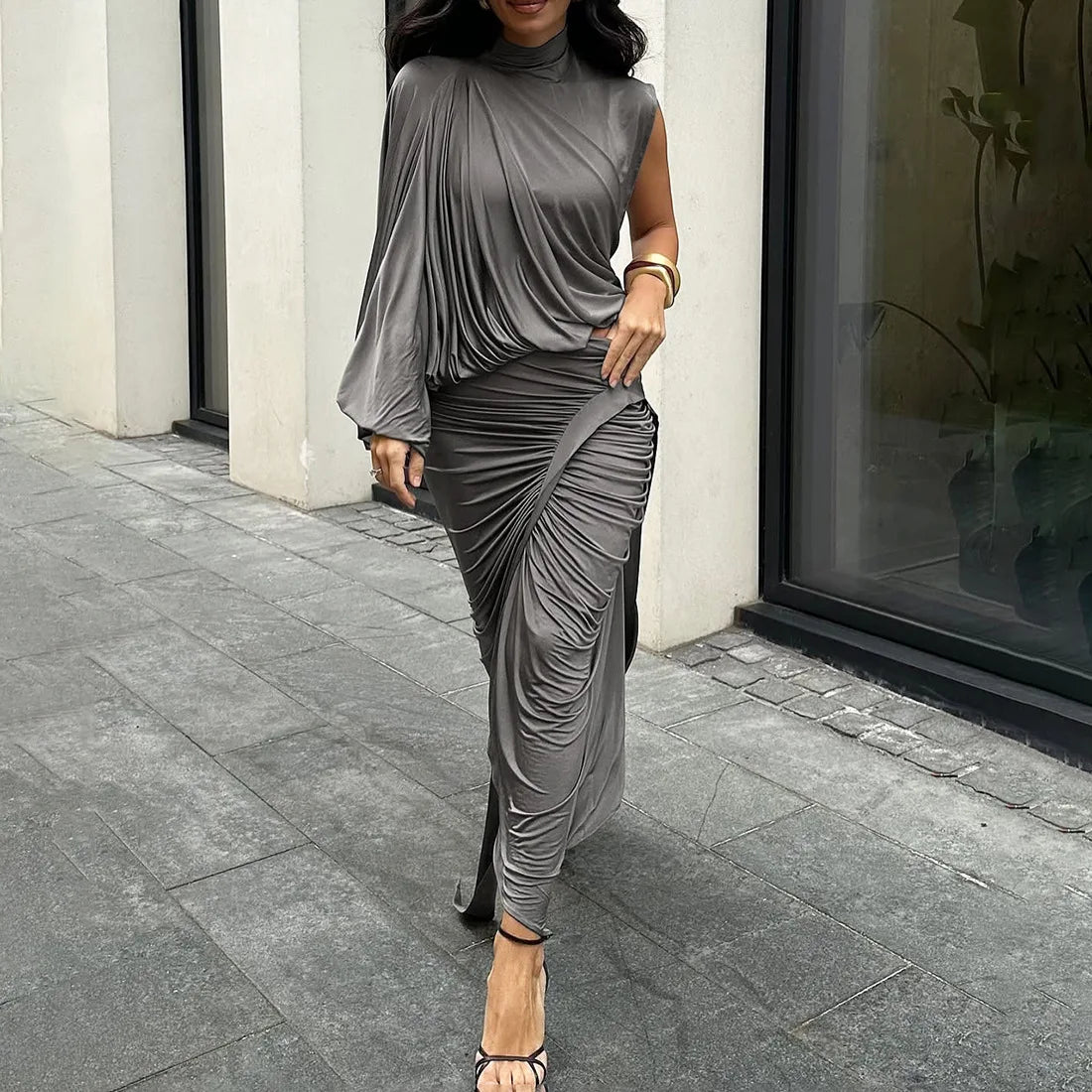 Woman wearing a gray draped dress walking on a sidewalk.