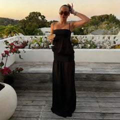 Woman in a black dress holding a drink on a rooftop with plants and sunset in the background