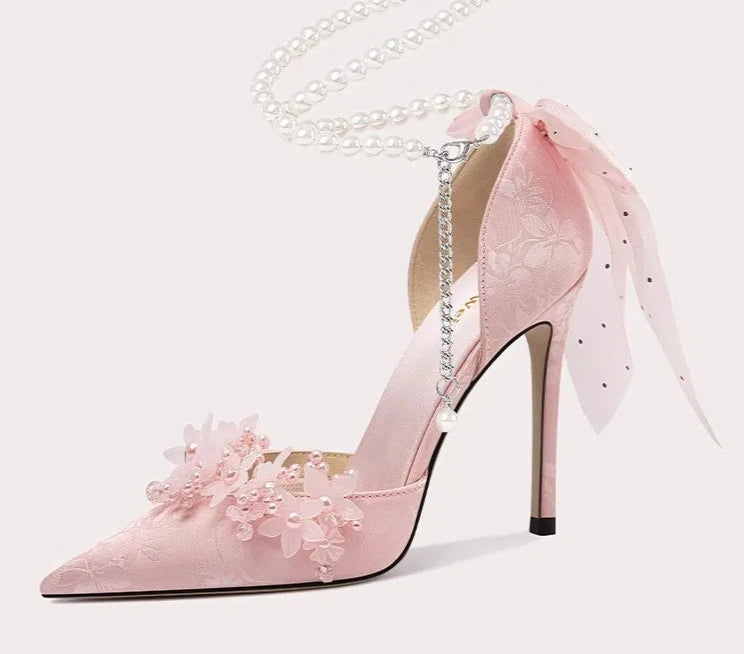Pink high-heeled shoe with floral details and a chain on a white background