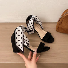Black polka-dot bow heels held by a hand