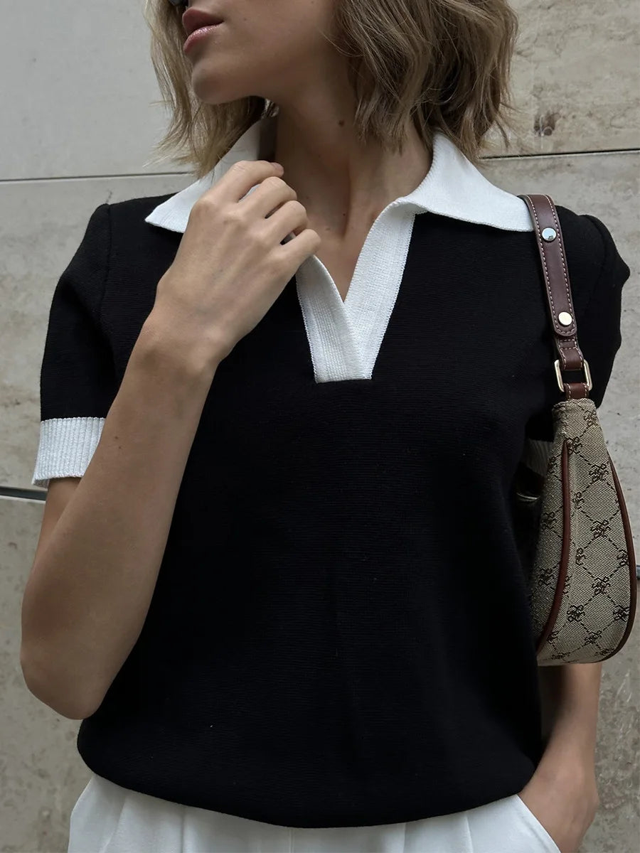 Woman wearing a black top with white collar and holding a patterned handbag against a neutral background