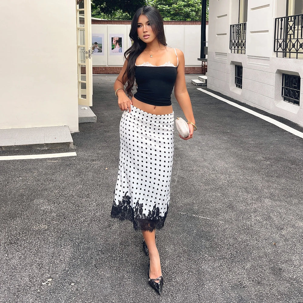 Woman in a black top and white polka dot skirt walking on a street.