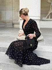Woman in a black polka dot dress sitting on steps holding a black handbag.