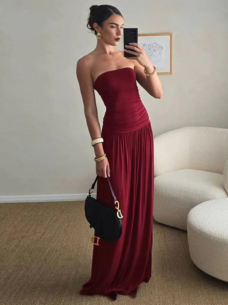 Woman in a burgundy strapless gown taking a mirror selfie in a room with a white couch.