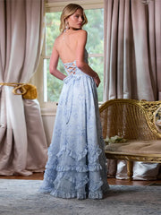 Woman in a light blue lace dress standing in a room with curtains and a wicker chair.