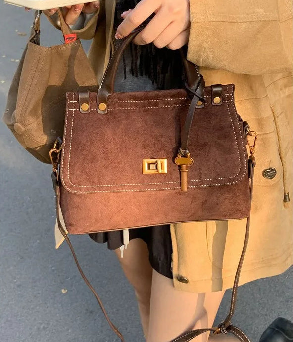 Brown leather handbag held by a person wearing a beige coat.