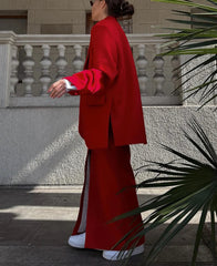 Person wearing a red outfit with white shoes standing against a stone wall.