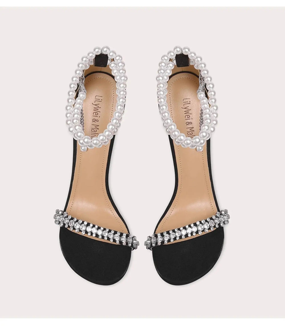 Black sandals with pearl and crystal embellishments on a light gray background
