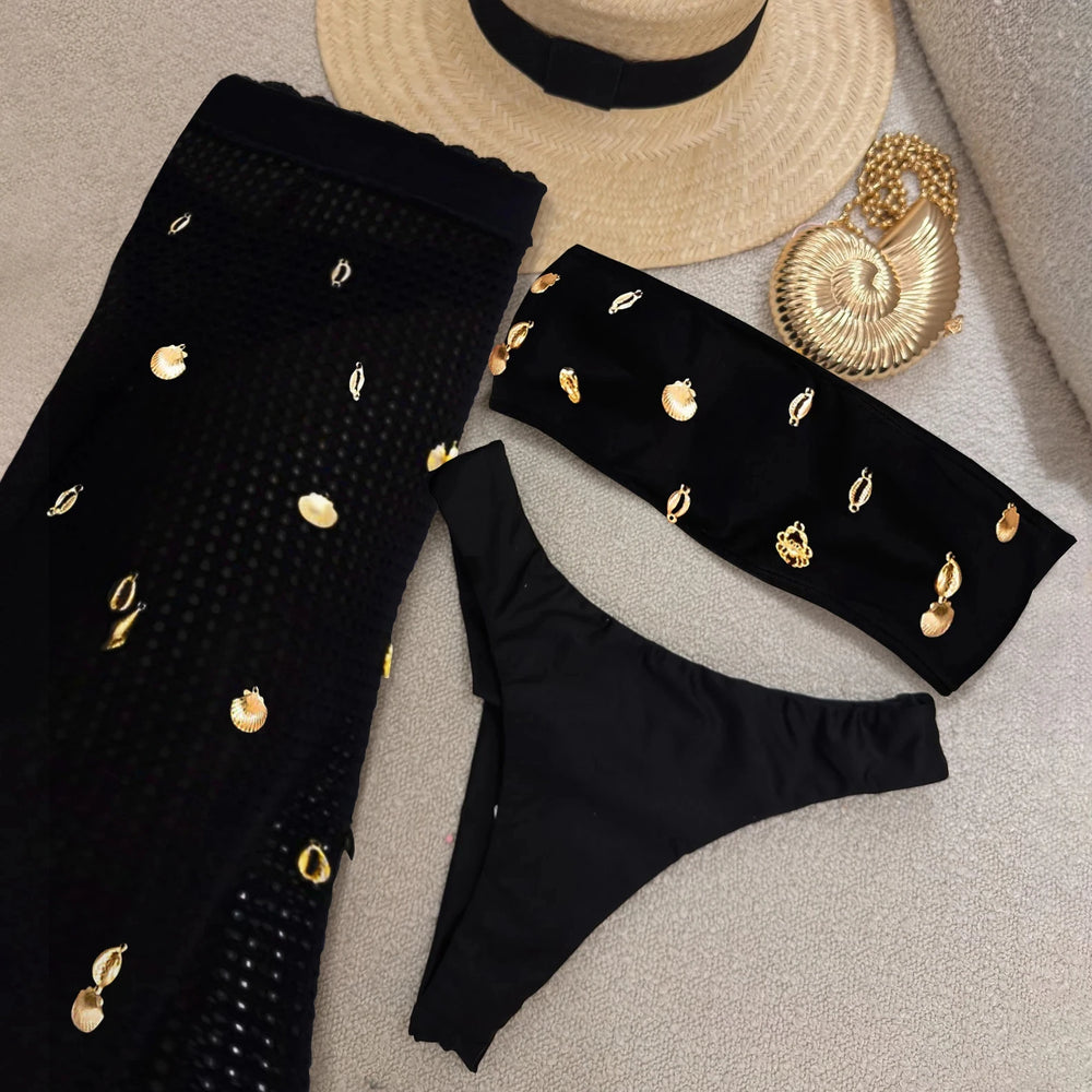 Flat lay of black bikini top, bikini bottom, and sheer cover-up pants with shell embellishments.