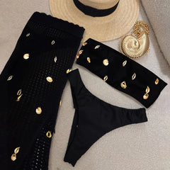 Flat lay of black bikini top, bikini bottom, and sheer cover-up pants with shell embellishments.